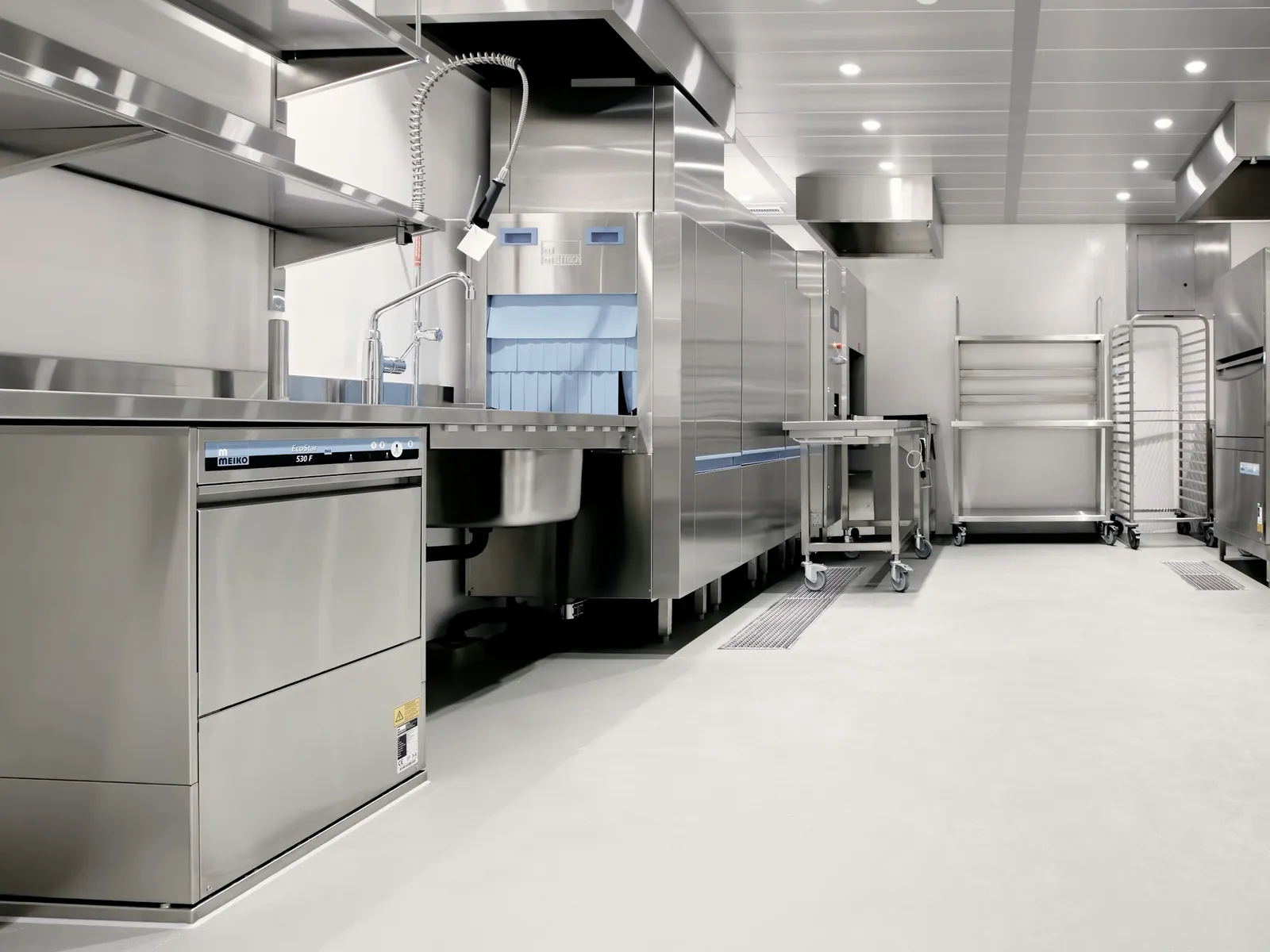 Stainless-steel commercial kitchen with a dish area, prep trolleys and a sealed floor